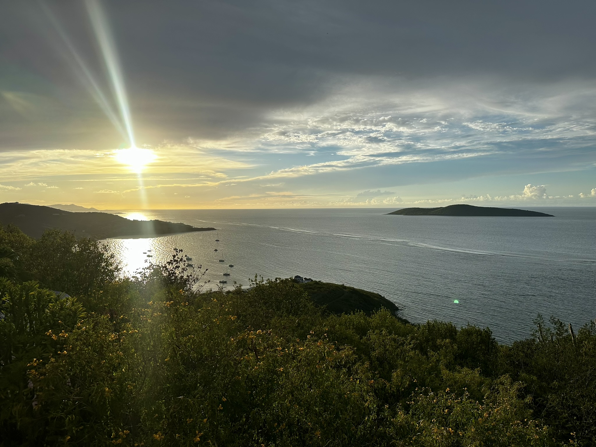 Golden evening light over an island bay with anchored sailboats and a green coastline