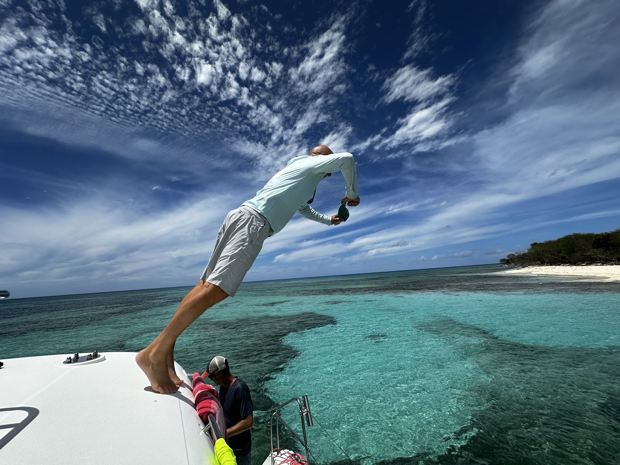 A guest jumping from the boat into clear turquoise water beside a sandy shoreline